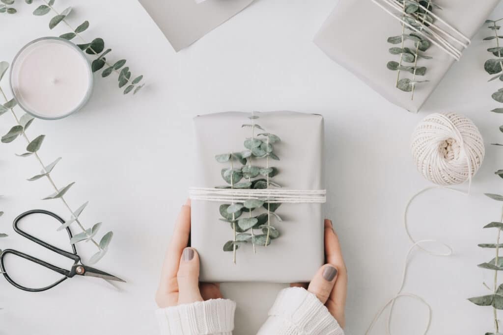 Girl's hands hold a gift box with minimalist style wrapping design. The concept of celebration events and wrapping gifts. Flat lay, top view.