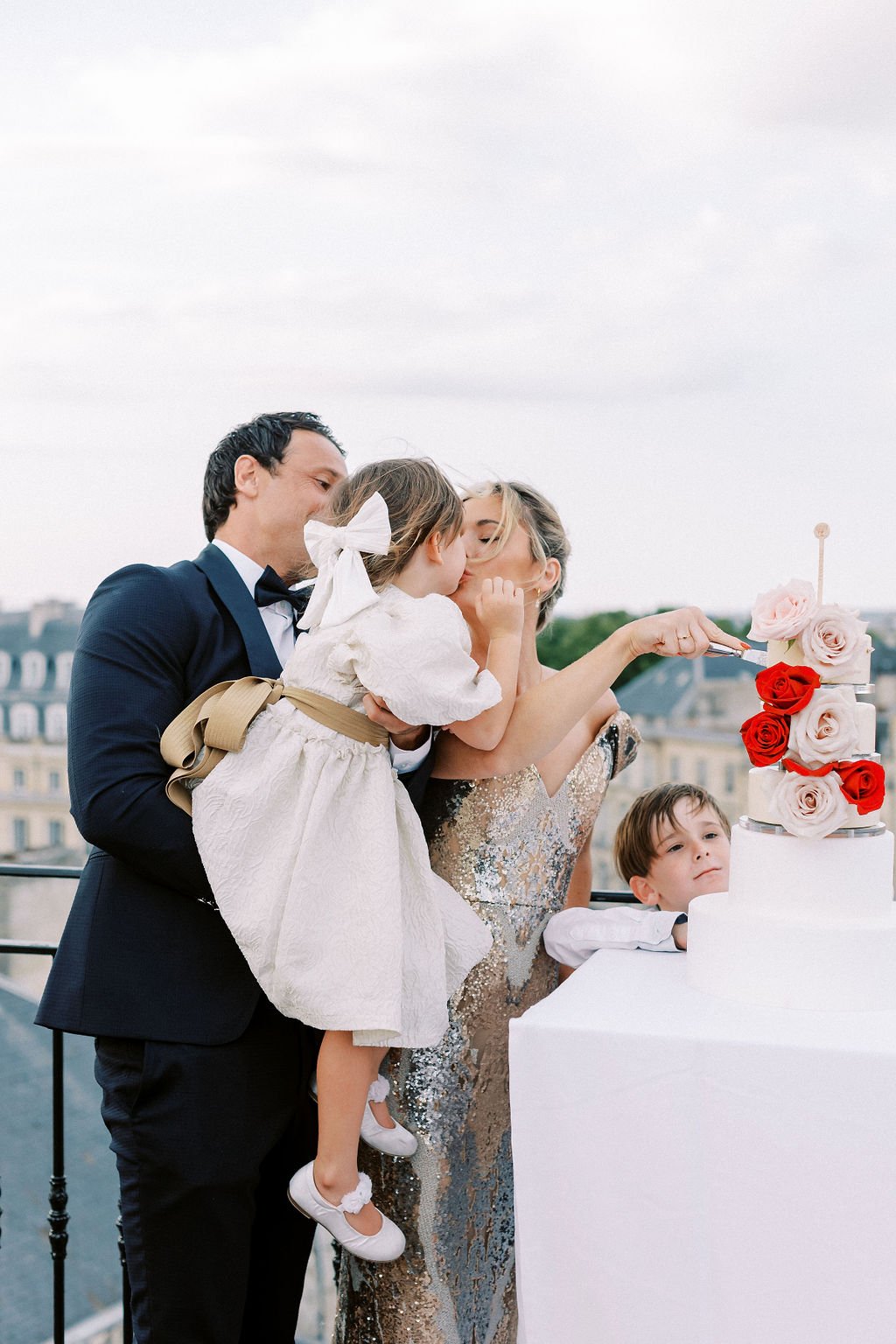 Bride kissing flower girl daughter while cutting modern cake