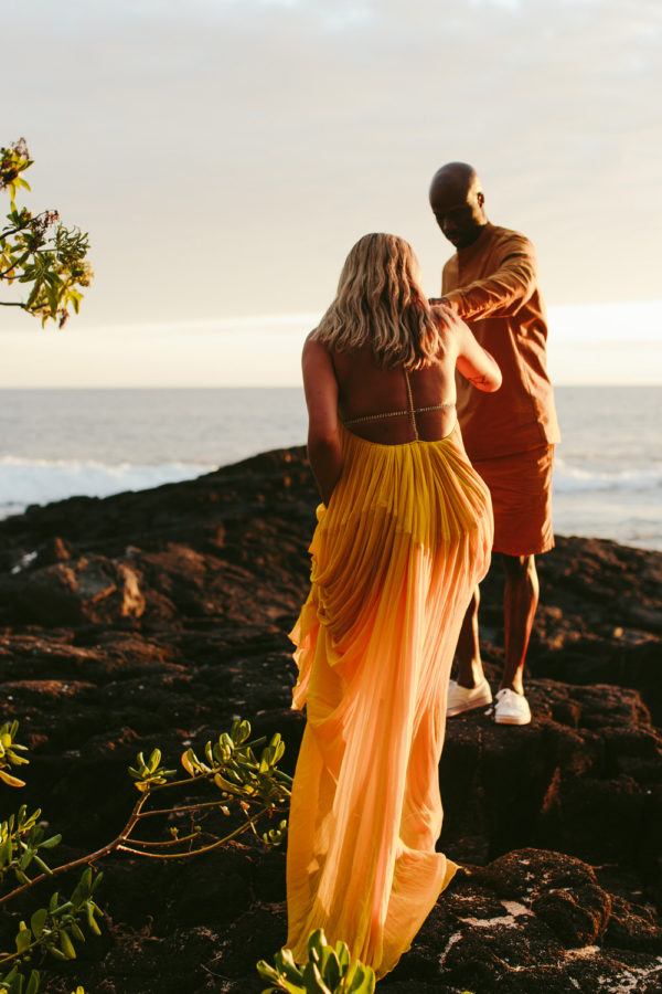 bride and groom climb the rocks in they vibrant yellow outfits