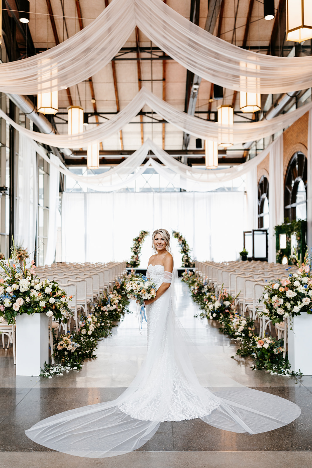 bride posing in front of peach and white flower lined aisle