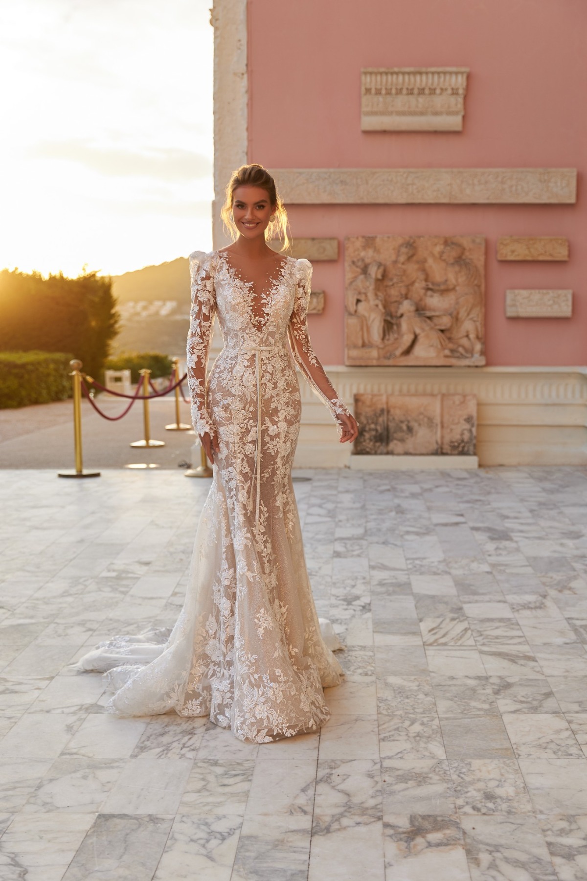 bride in long sleeve wedding dress in front of pink wedding venue