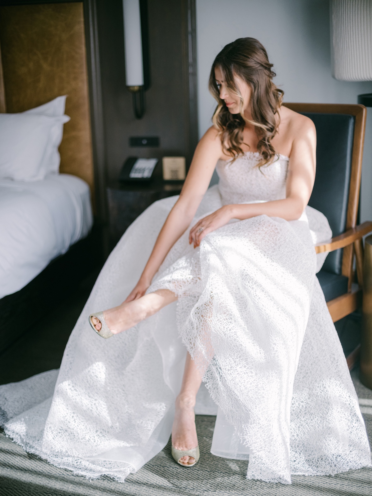 bride in modern lace wedding gown putting on shoes