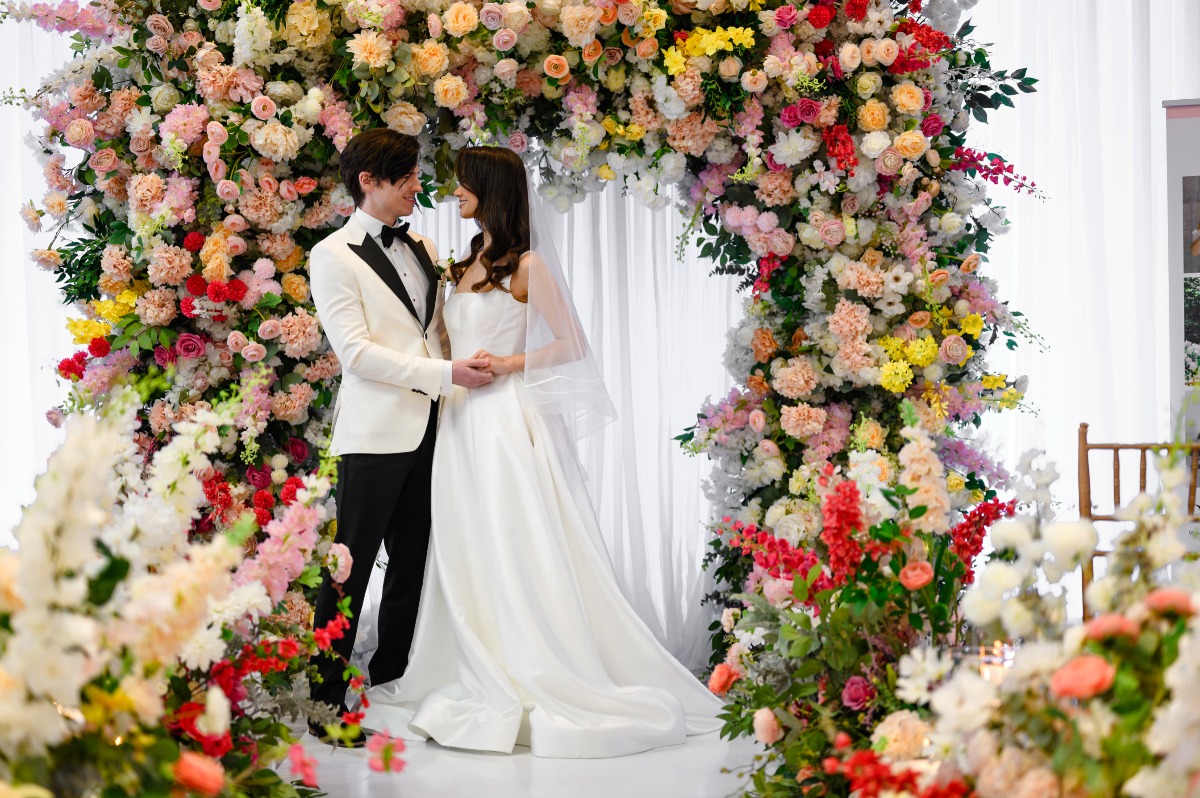 couple in front of big colorful ceremony backdrop full of flowers