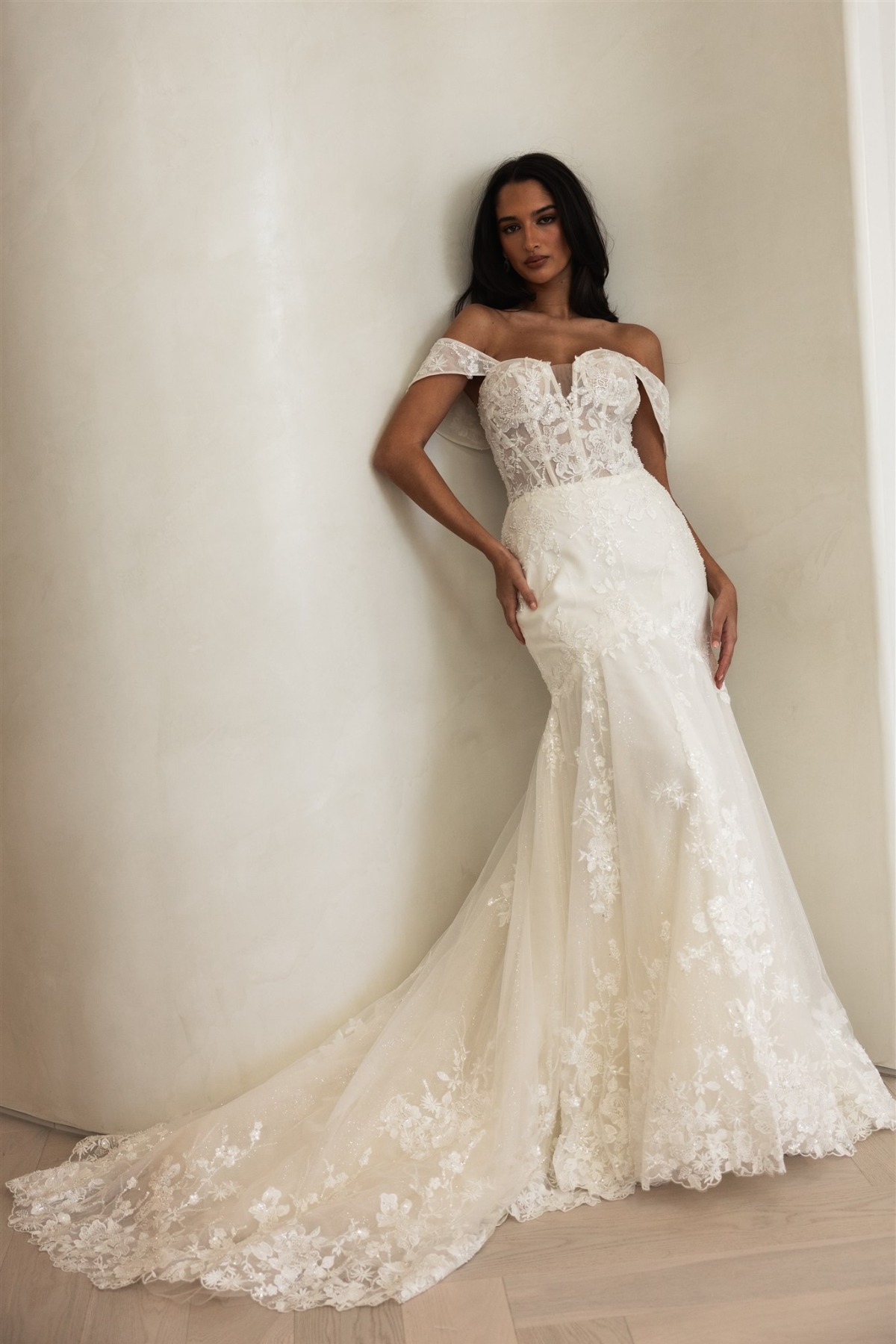 bride leaning against wall in off shoulder wedding dress